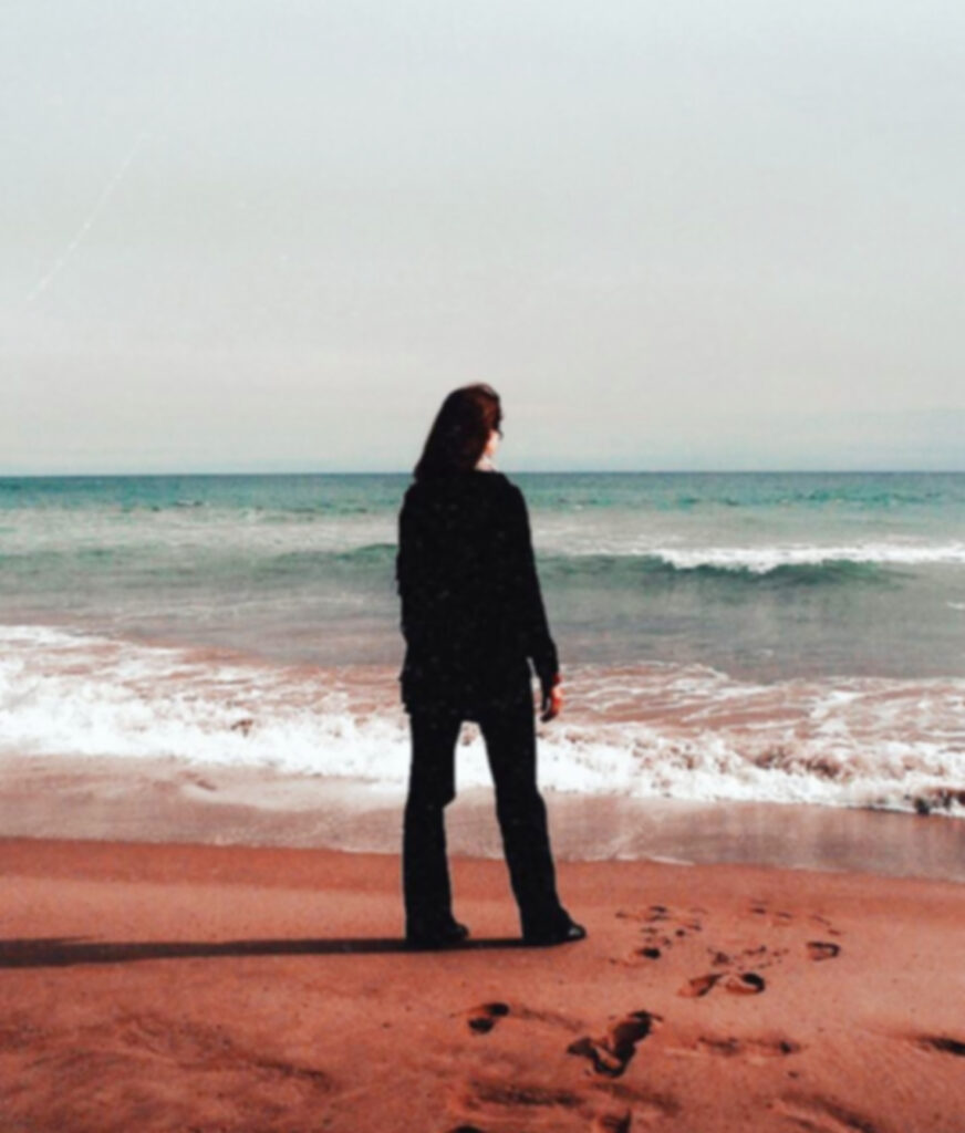 Frau am Strand schaut raus aufs Meer
